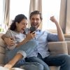 Overjoyed,Surprised,Young,Couple,Looking,At,Phone,Screen,,Reading,Message