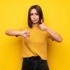 Young,Woman,Over,Yellow,Wall,Making,Good-bad,Sign.,Undecided,Between
